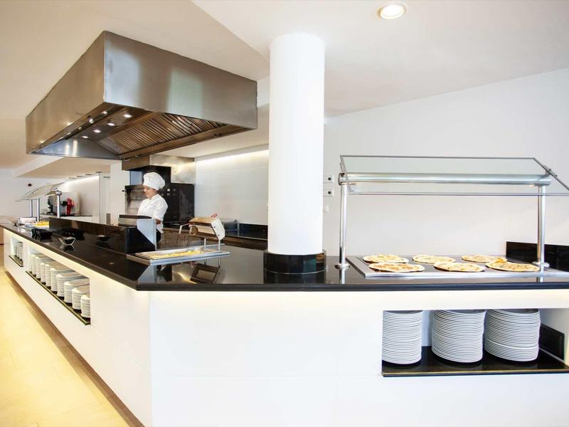 Cuisine d'hôtel moderne avec espace buffet et chef préparant des plats.