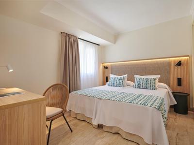 Jasny pokój hotelowy z łóżkiem podwójnym, biurkiem, krzesłem i oknem z zasłonami.