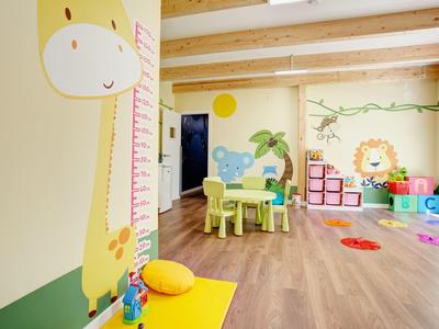 Jasny, przyjazny dla dzieci pokój zabaw z drewnianą podłogą, kolorowymi meblami i motywami zwierząt na ścianach.