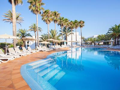 Groot buitenzwembad met ligstoelen en palmbomen onder een heldere hemel.