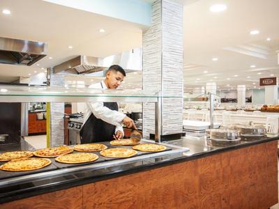 Mężczyzna podaje pizzę przy bufecie w jasnej, nowoczesnej restauracji hotelowej.