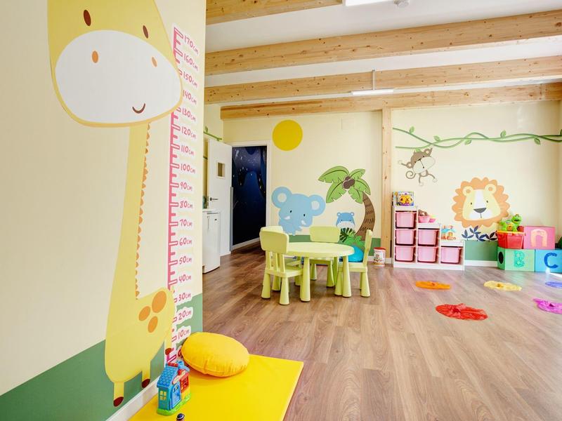 Jasny, przyjazny dla dzieci pokój zabaw z drewnianą podłogą, kolorowymi meblami i motywami zwierząt na ścianach.