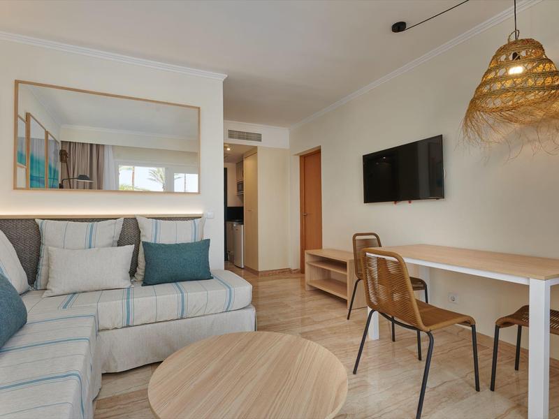 Nowoczesny salon z narożną sofą, telewizorem i stołem z dwoma krzesłami.