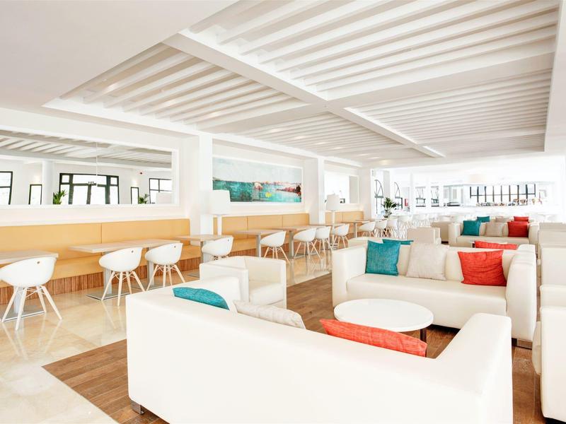 Jasny salon hotelowy z białymi sofami i kolorowymi poduszkami, nowoczesna atmosfera miejska.