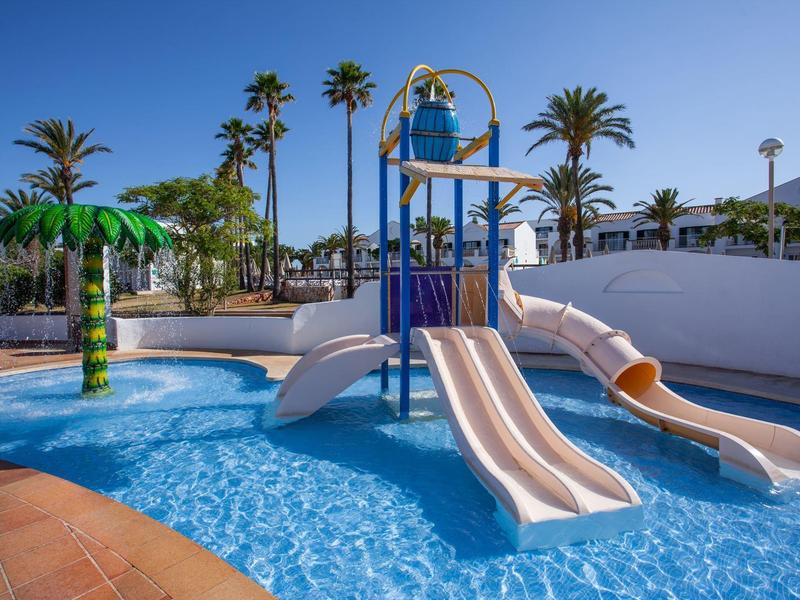 Dziecięcy park wodny z zjeżdżalniami, brodzikiem i palmami pod niebieskim niebem