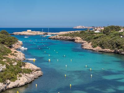 Przejrzysty niebieski przesmyk morskiego z żółtymi bojami między zielonymi skalistymi klifami pod niebieskim niebem.