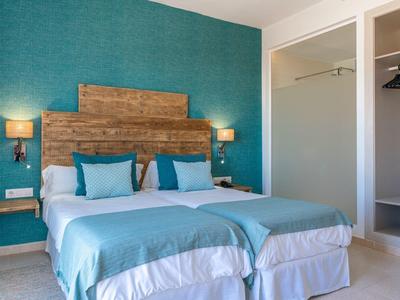 Nowoczesny pokój hotelowy z dwoma łóżkami, turkusowymi ścianami i minimalistycznym wystrojem.