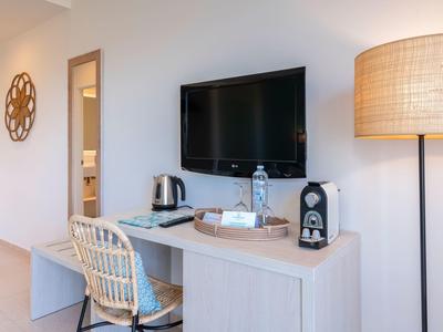 Nowoczesna część pokoju hotelowego z biurkiem, krzesłem, telewizorem, czajnikiem i lampą stojącą.