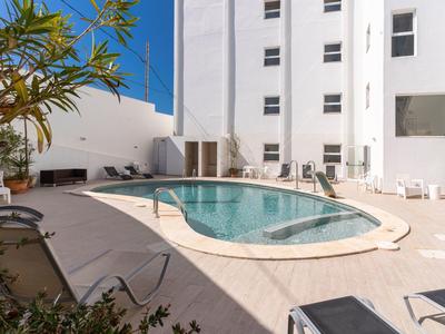 Nowoczesny basen hotelowy z leżakami i białymi ścianami pod niebieskim niebem.