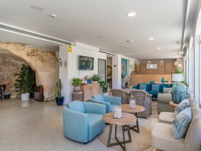 Jasna część wypoczynkowa hotelu z wygodnymi fotelami, sofami, drewnianymi stolikami, jasną podłogą i dużymi oknami.