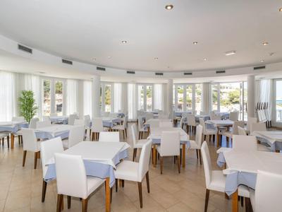 Jasna i nowoczesna restauracja z dużymi oknami i stołami przykrytymi białymi obrusami.