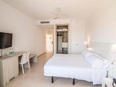 Jasny pokój hotelowy z podwójnym łóżkiem, biurkiem, krzesłem i telewizorem z płaskim ekranem.