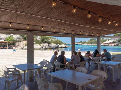 Strefa siedząca kawiarni na plaży z widokiem na piaszczystą plażę i morze w słoneczny dzień.