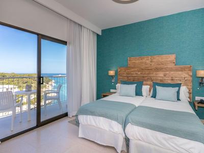 Camera d'hotel con due letti, parete turchese e vista su balcone e mare.