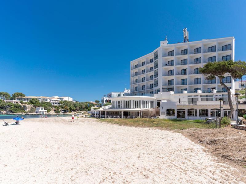 Wielopiętrowy hotel z basenem na piaszczystej plaży pod bezchmurnym niebem