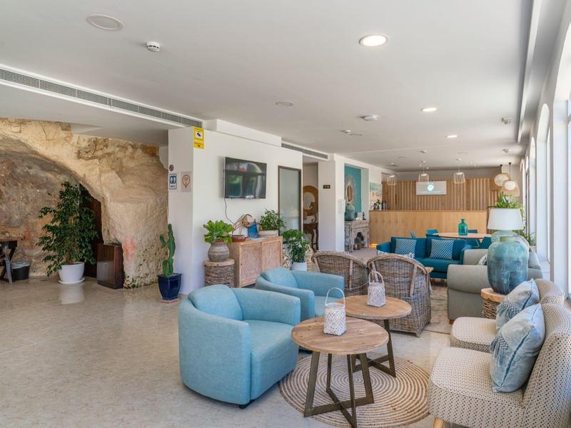 Jasna część wypoczynkowa hotelu z wygodnymi fotelami, sofami, drewnianymi stolikami, jasną podłogą i dużymi oknami.