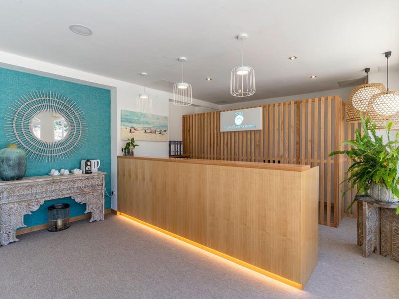 Jasna recepcja hotelowa z drewnianym biurkiem, zieloną ścianą akcentową i roślinami dekoracyjnymi.