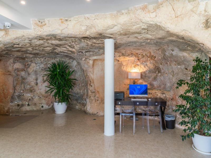 Stanowisko komputerowe w pokoju jaskiniowym z roślinami i kamiennymi ścianami.