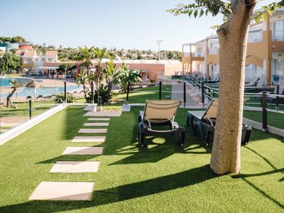 Giardino dell'hotel con sdraio, prato, albero e vista su piscina e edifici.