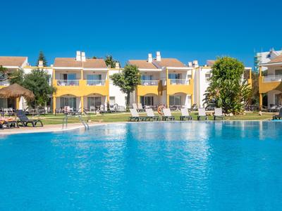 Appartamenti gialli con terrazze accanto a una grande piscina blu sotto un cielo limpido.