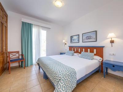 Camera luminosa con letto matrimoniale, comodini blu e grande armadio in legno.