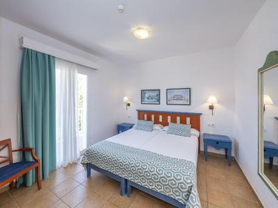 Camera d'hotel luminosa con letto matrimoniale, mobili blu e tenda verde vicino al balcone