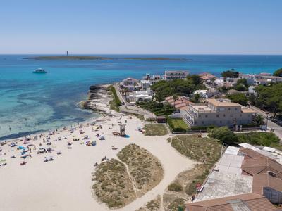 Veduta aerea di una spiaggia sabbiosa bianca, mare blu e villaggio adiacente.