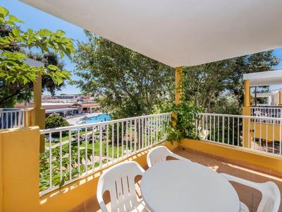 Balcone con tavolo bianco e sedie, vista su alberi e edifici vicini.