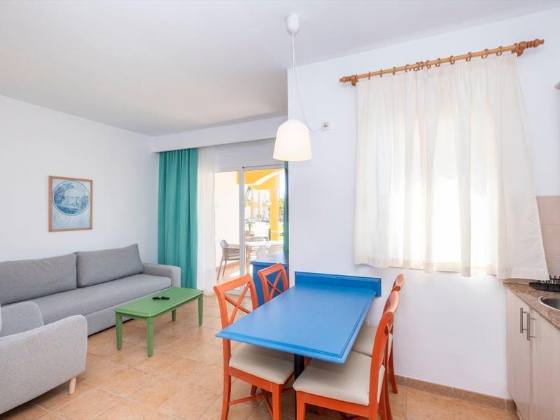 Soggiorno luminoso con tavolo da pranzo, sedie, divano grigio e vista sul balcone e sul mare.