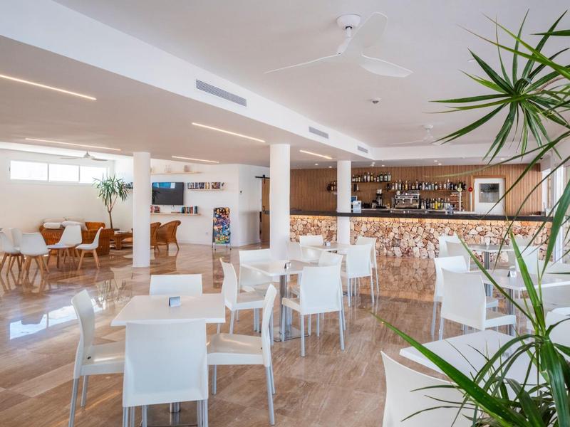 Ristorante luminoso e moderno con sedie bianche, tavoli in legno e accenti di piante.