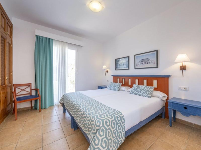 Camera luminosa con letto matrimoniale, comodini blu e grande armadio in legno.