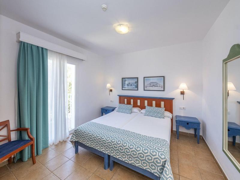 Camera d'hotel luminosa con letto matrimoniale, mobili blu e tenda verde vicino al balcone