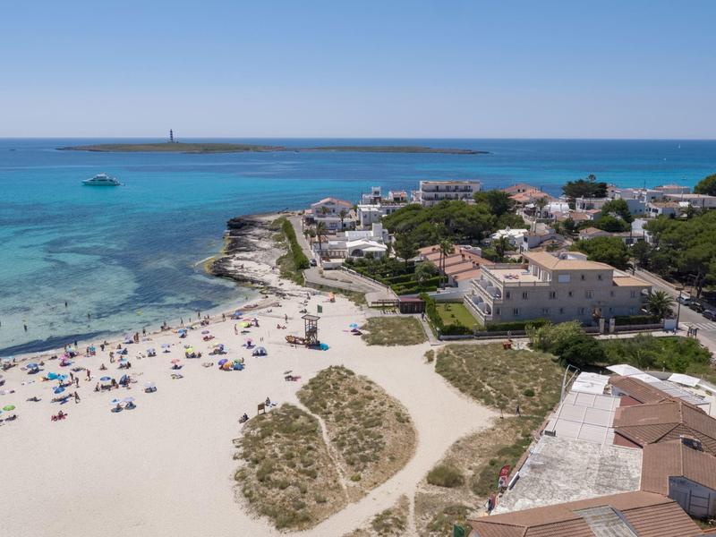 Veduta aerea di una spiaggia sabbiosa bianca, mare blu e villaggio adiacente.