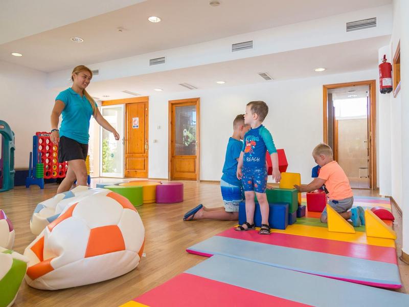 Bambini che giocano su tappeti colorati in una stanza giochi luminosa e moderna dell'hotel.