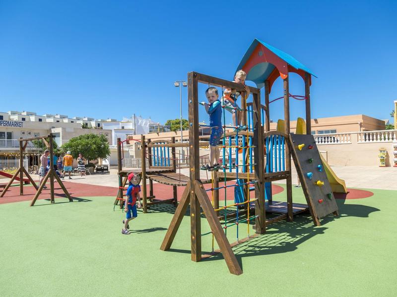 Bambini che giocano su una struttura per arrampicata con scivolo in un parco giochi sotto un cielo blu.