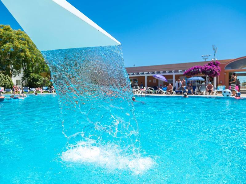 Cascata nella piscina blu dell'hotel con persone e edifici sullo sfondo sotto il sole
