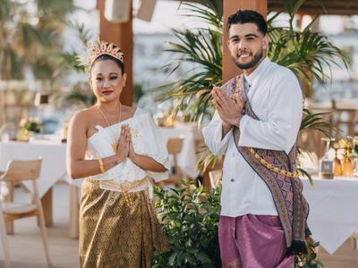 A traditionally dressed couple welcomes in an open restaurant setting with green decorations.