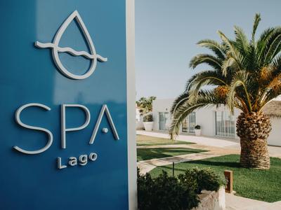 Blue SPA Lago sign next to a palm tree and manicured garden under clear sky