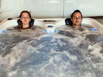 Two people relax in a bubbling hot tub with headrests.