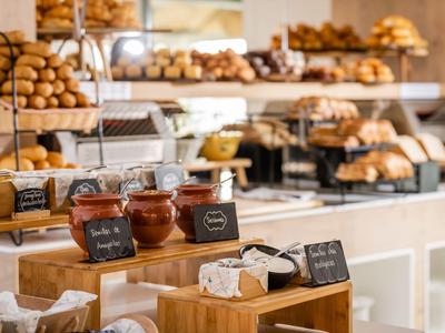 Varied breakfast buffet with jams, rolls, and pastries on wooden furniture.