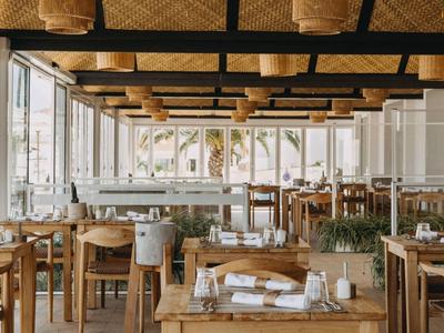 Brightly decorated restaurant with wooden chairs and large windows overlooking palm trees.