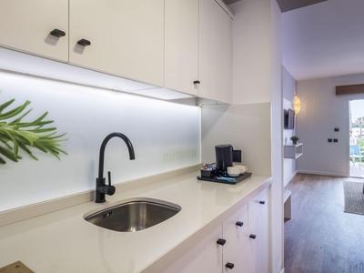 Modern kitchenette with black faucet, white countertop, and access to living room