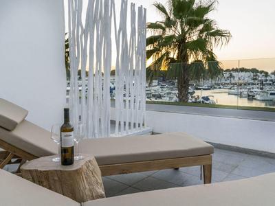 Sun loungers with wine bottle on balcony overlooking harbor and palm trees at sunset.