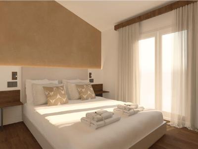 Modern hotel room with large bed, decorative pillows, and daylight through windows.