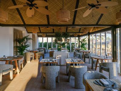 Área de comedor luminosa del hotel con muebles de madera y grandes ventanas con vista al exterior.