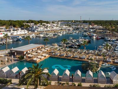 Gran piscina del hotel con tumbonas con vistas a una marina llena de yates y barcos.