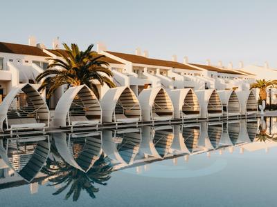 Habitaciones de hotel blancas modernas con camas redondas privadas junto a la piscina al atardecer.
