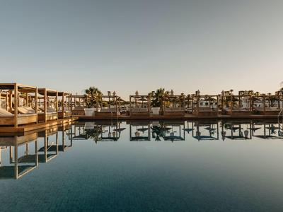 Piscina lujosa de hotel con tumbonas y palmeras al atardecer.