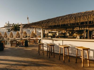 Bar de playa abierta con techo de paja y taburetes de madera al atardecer.