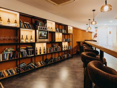Vestíbulo de hotel moderno con estanterías, taburetes de bar y luz cálida.